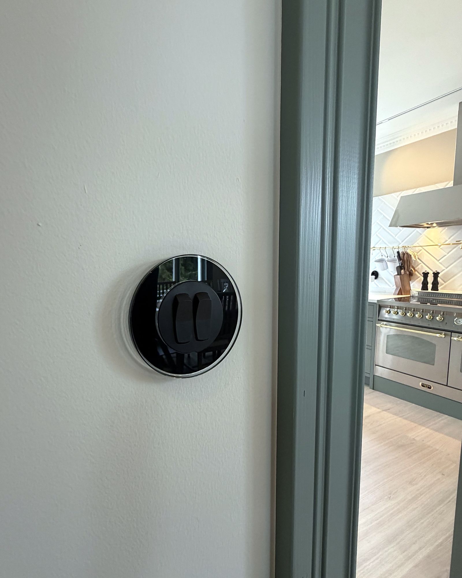 Rund strömbrytare i svart glas vid dörren till ett kök